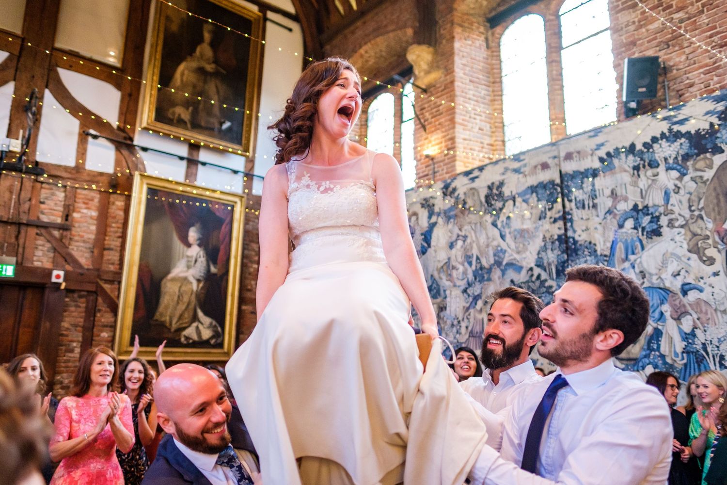 Wedding reception celebration with guests dancing and cheering in a rustic brick venue.