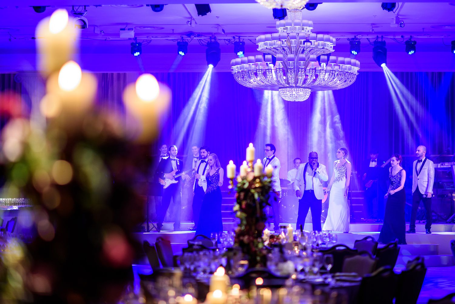 Elegant ballroom with crystal chandelier and purple lighting during wedding celebration.