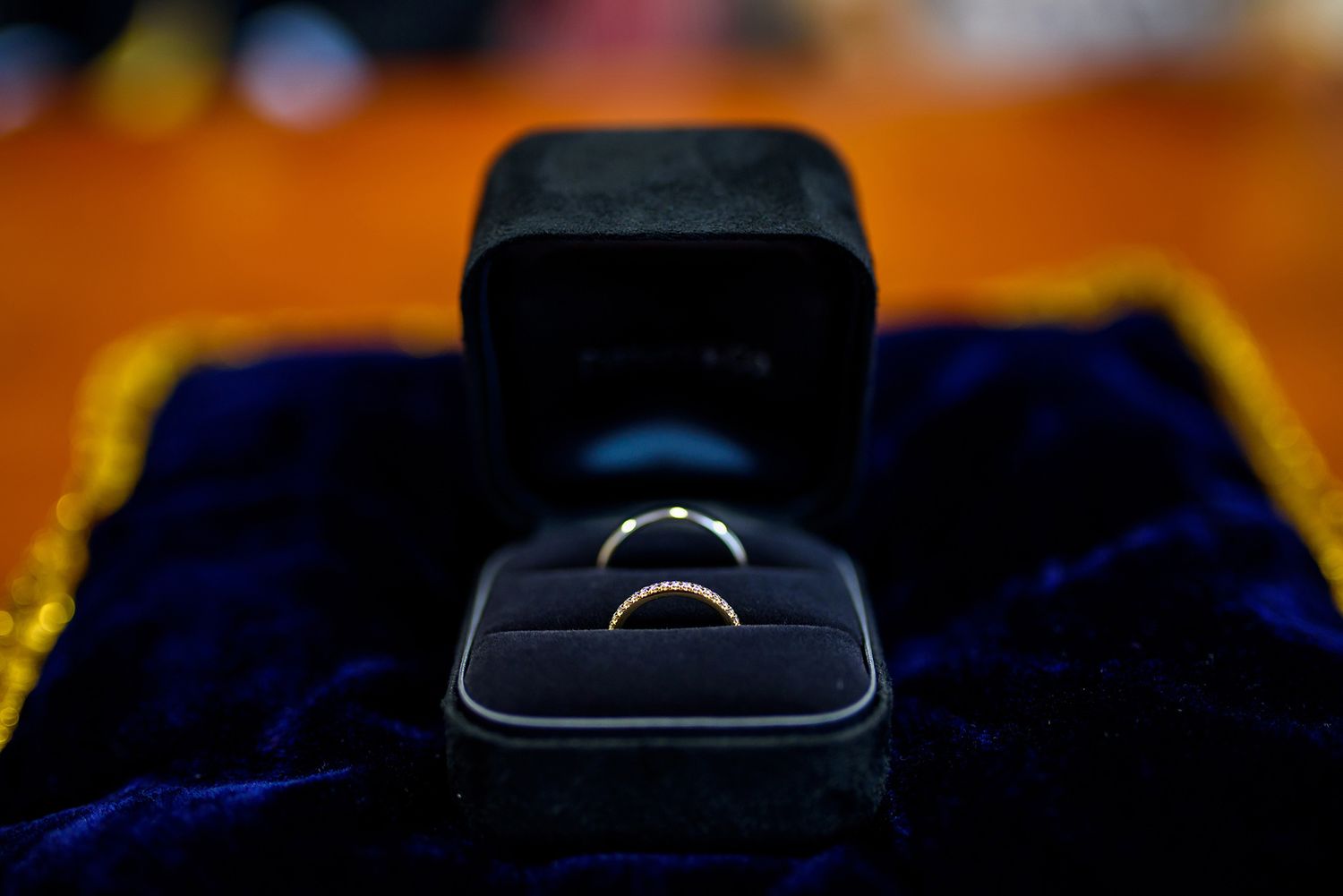 Wedding rings displayed on dark blue fabric with dramatic lighting.
