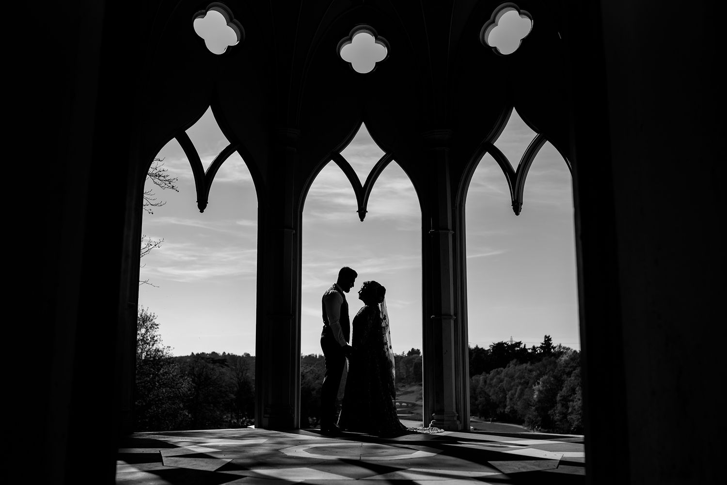 Silhouettes framed by Gothic arched windows in dramatic black and white.