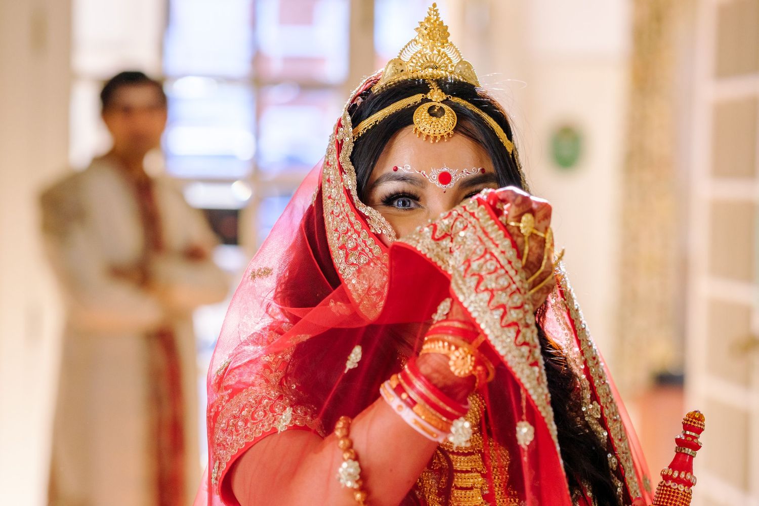 Traditional Indian wedding ceremony with bride in red lehenga and groom in white sherwani performing rituals.