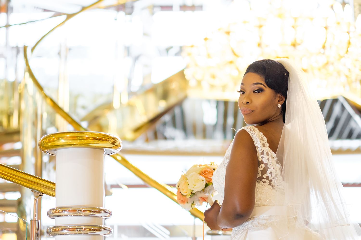 Bride holding bouquet poses against golden carousel columns.