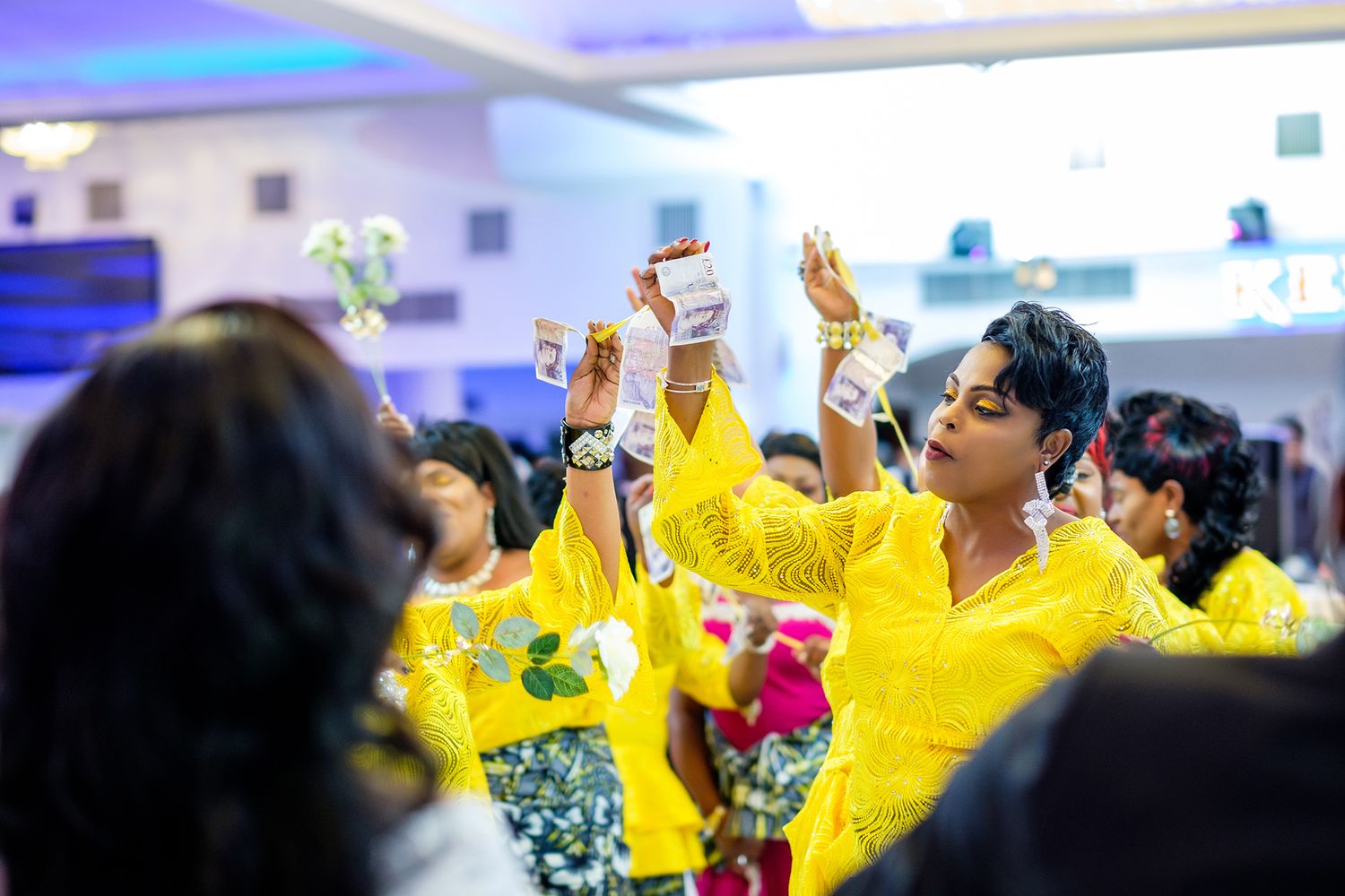 Wedding guests in bright yellow attire dancing with raised hands during celebration.