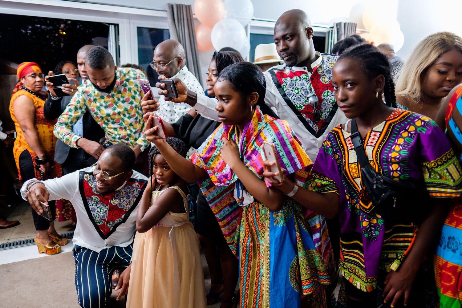 Party guests in colorful African print outfits dancing together in a line formation.