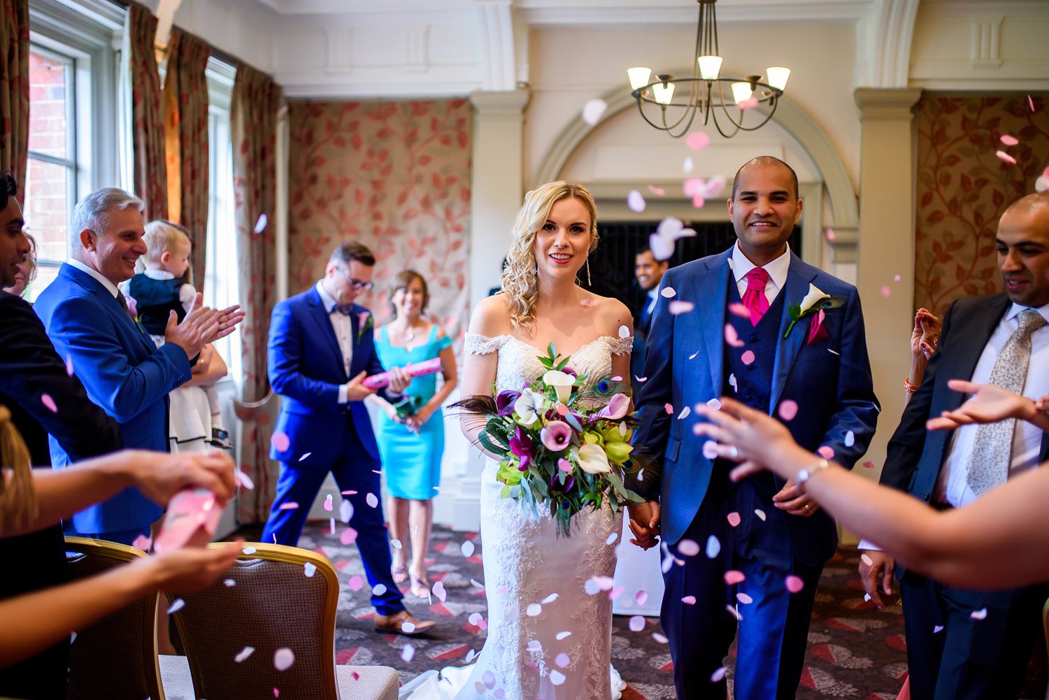 Wedding guests gather in an elegant room with floral wallpaper for celebration.