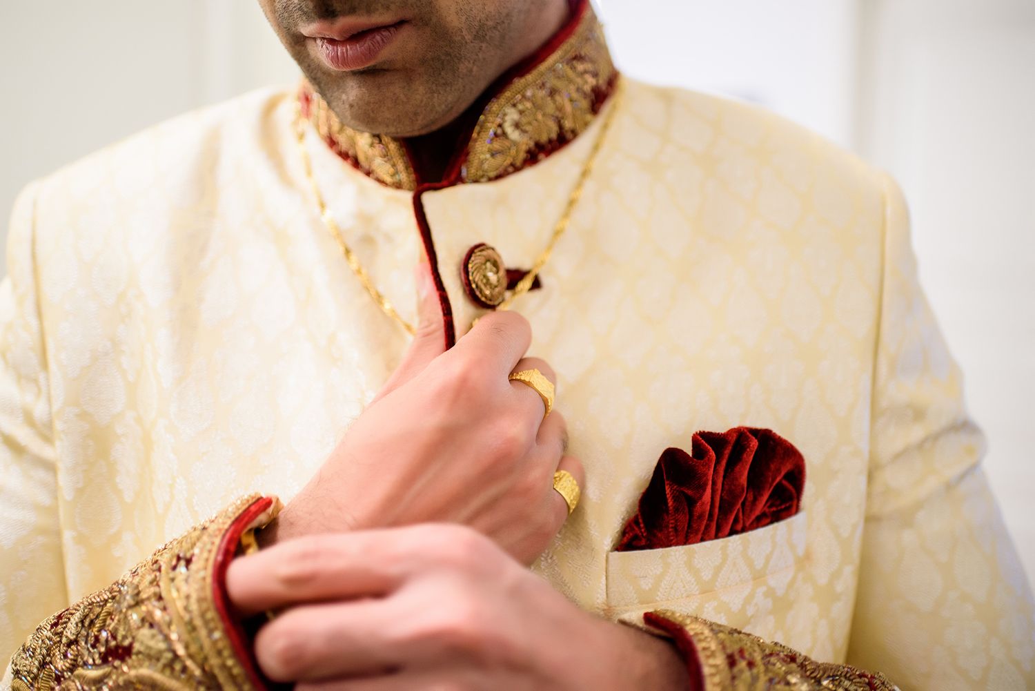 Close-up detail of an ornate cream and gold traditional wedding sherwani with red pocket square.