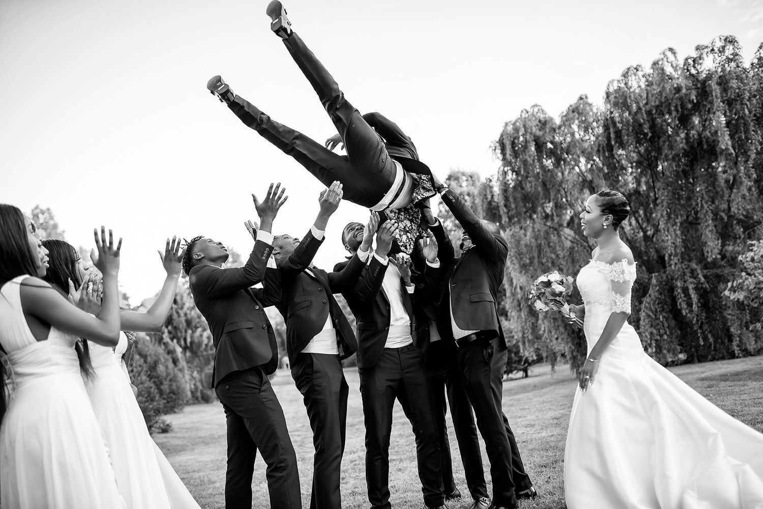 Black and white photo of wedding party jumping and posing outdoors.