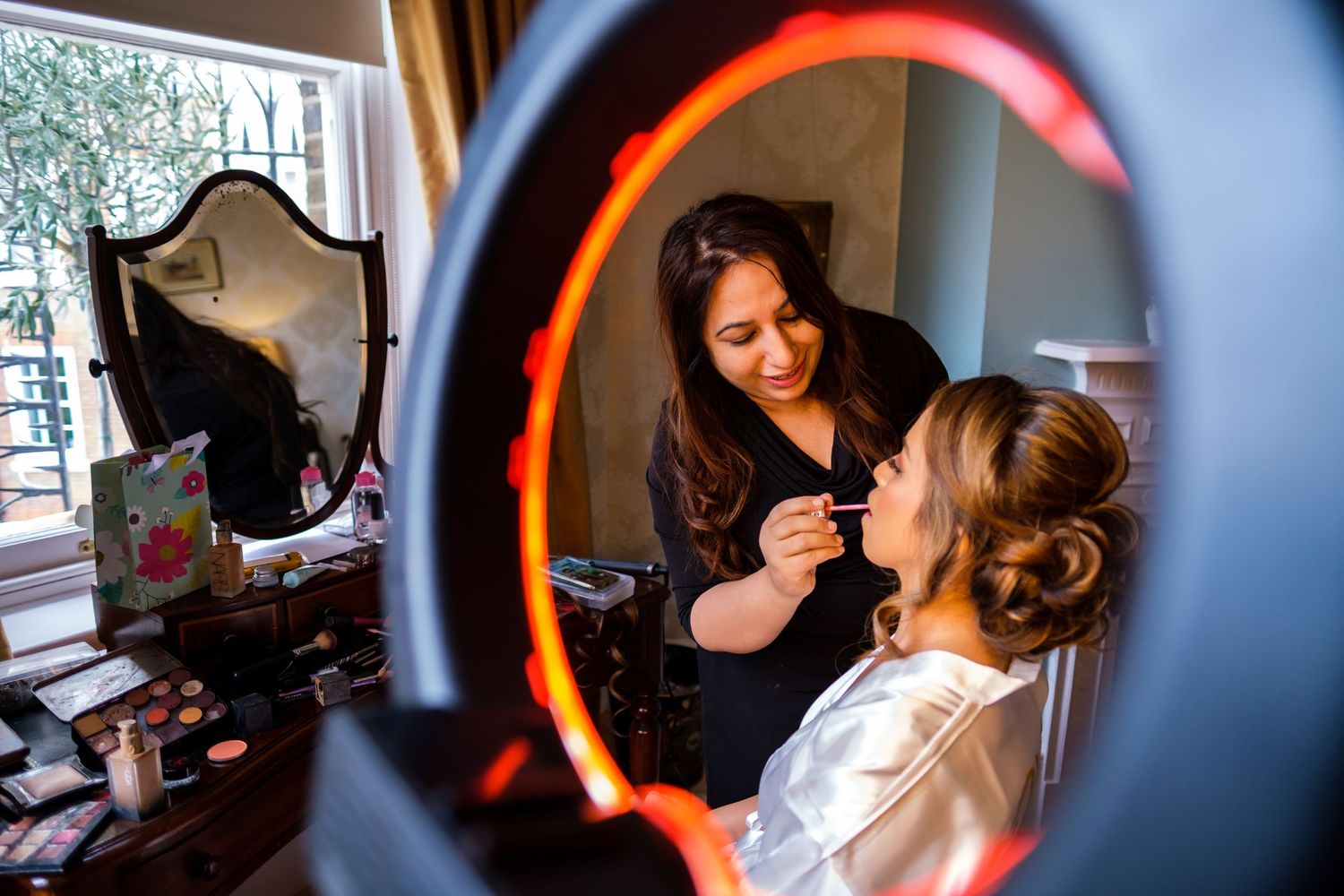 Professional makeup artist applies cosmetics to client in elegant preparation room with warm lighting.