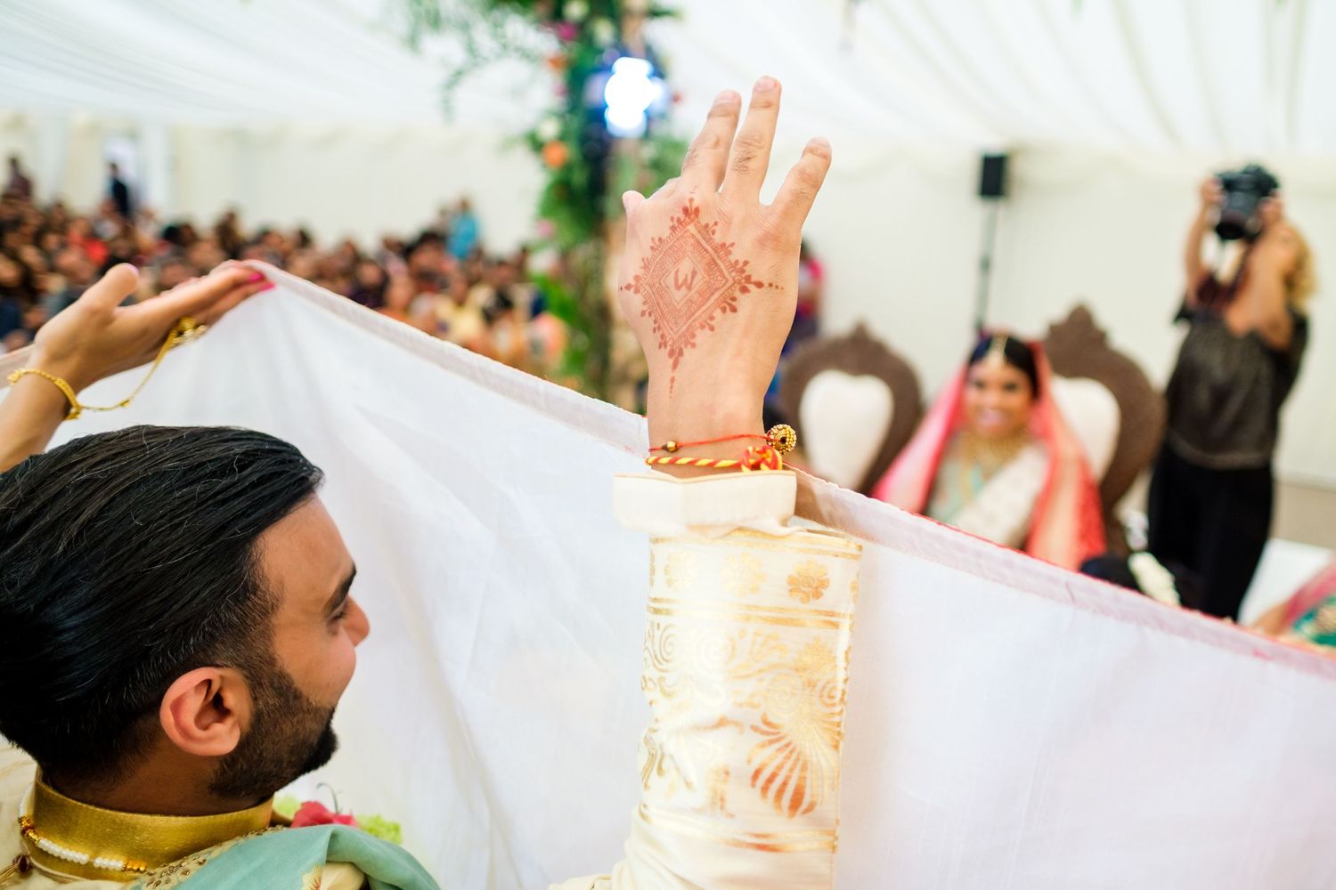 Hand with henna design raised during traditional Indian wedding ceremony.