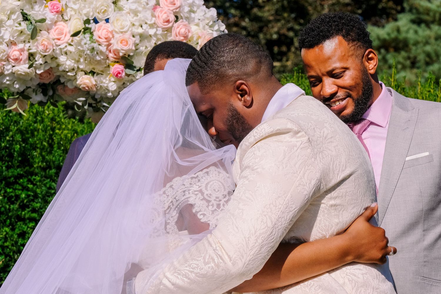 Wedding ceremony moment captured outdoors with pink floral decorations and natural greenery in the background.