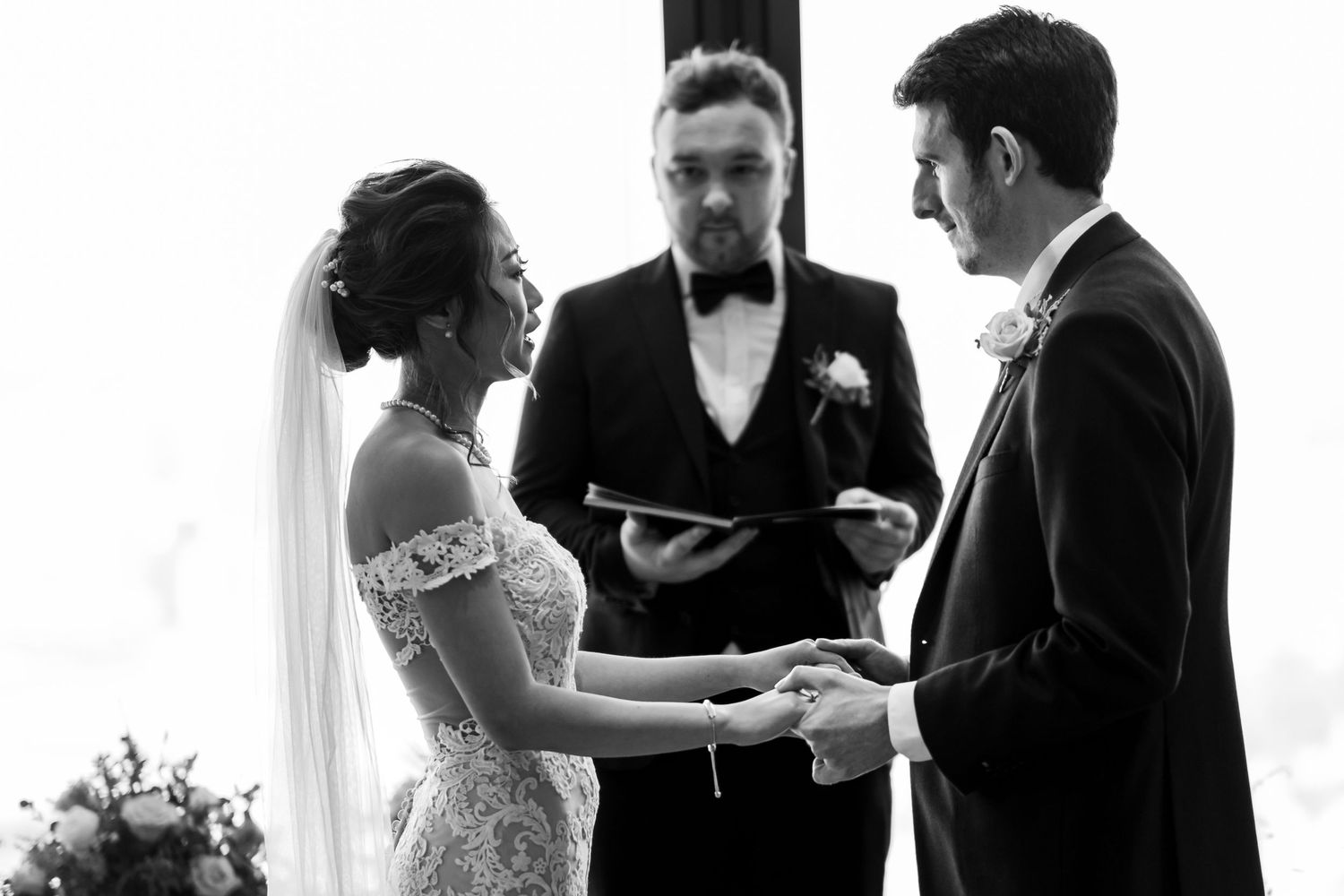 Wedding party members in formal attire gather around to sign documents during an elegant indoor ceremony.