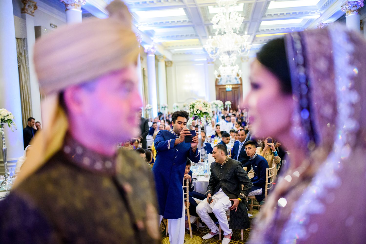 Wedding celebration in an ornate hall with decorative ceiling and chandeliers.