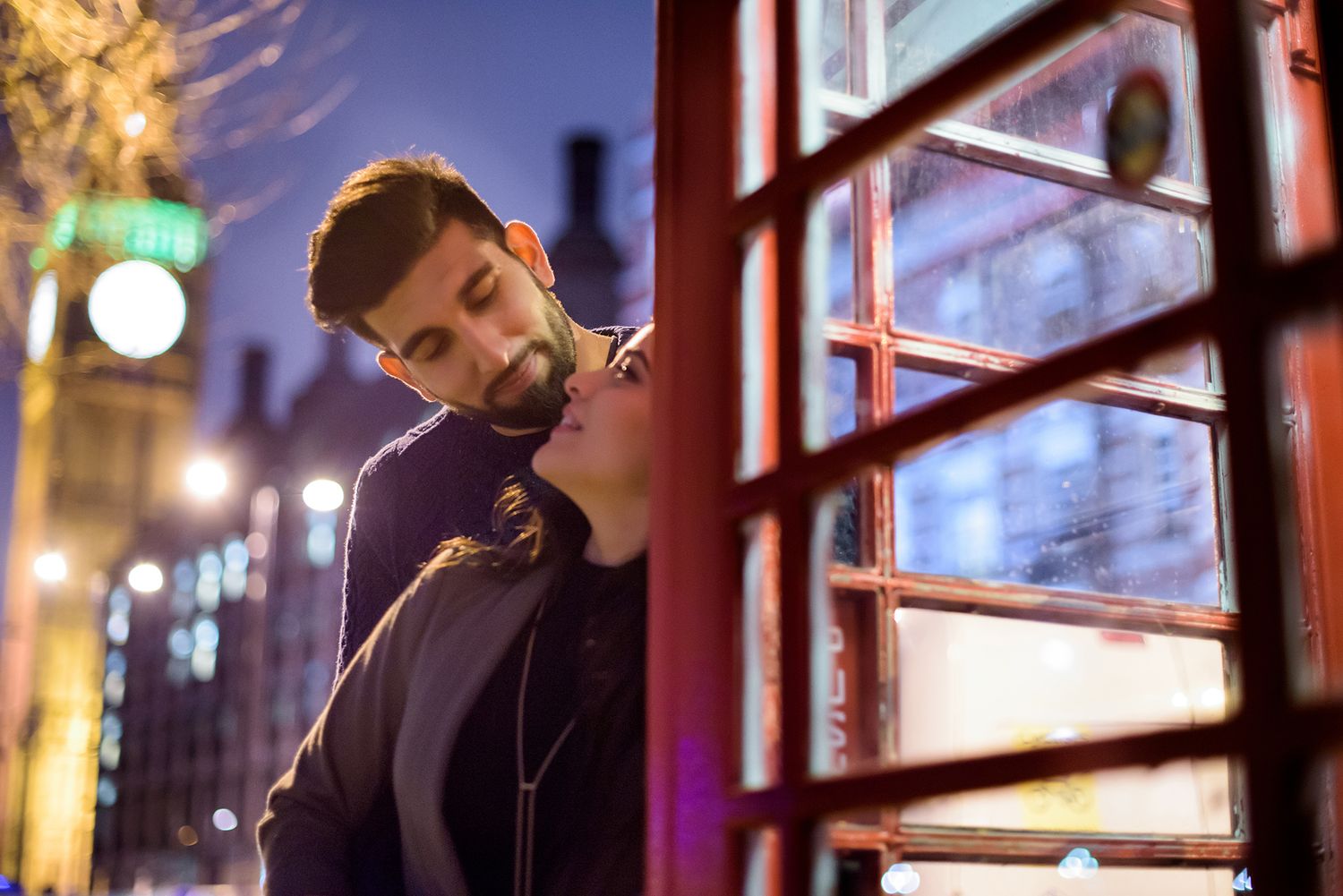Intimate moments captured inside vintage red London phone booth at night.