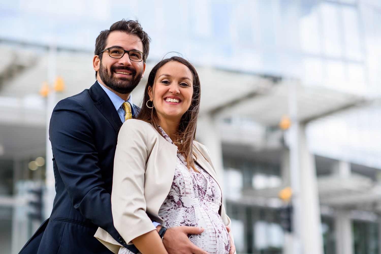 Couple posing outdoors near modern glass building in urban setting.