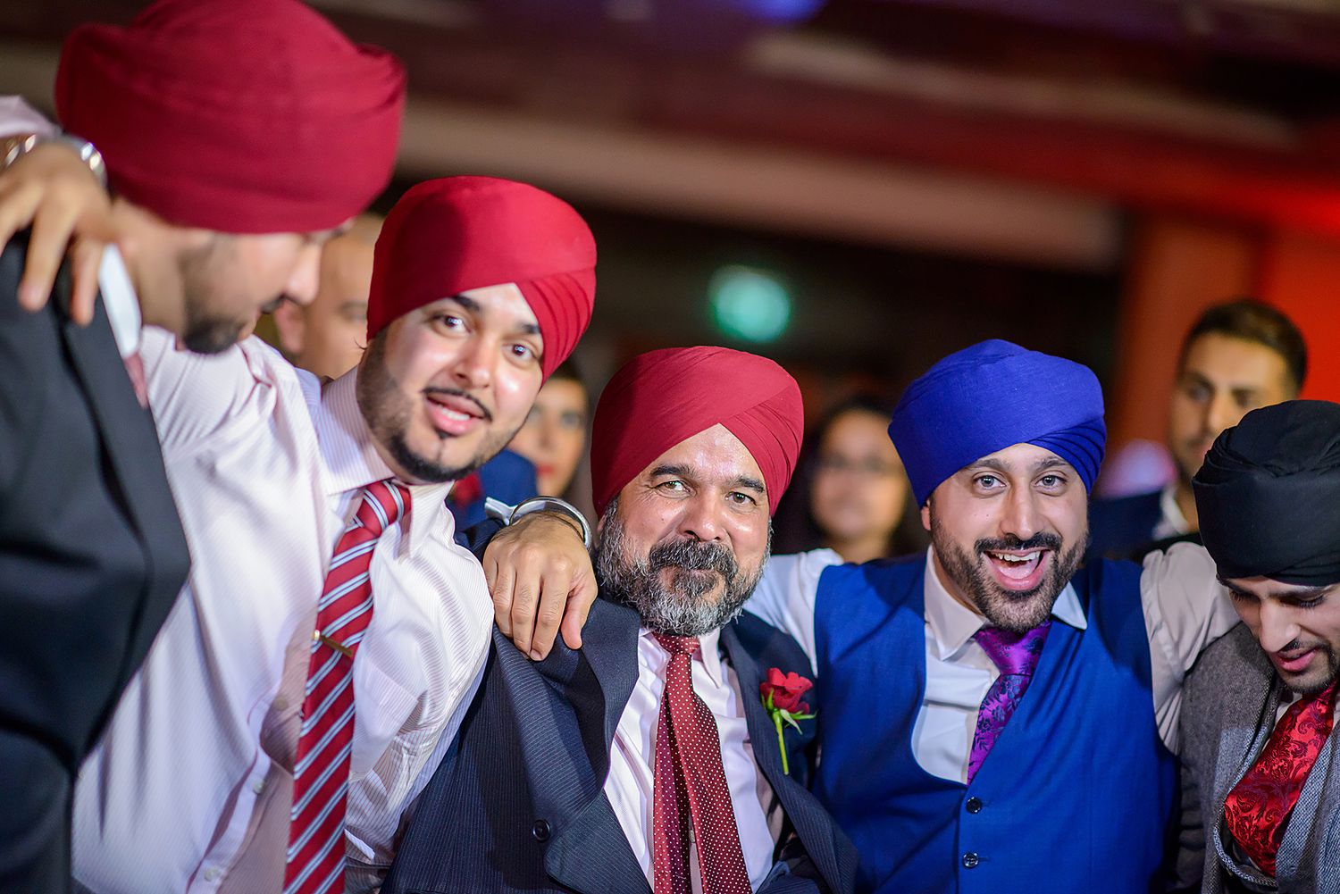 Wedding guests wearing formal attire and traditional Sikh turbans celebrating at a reception.