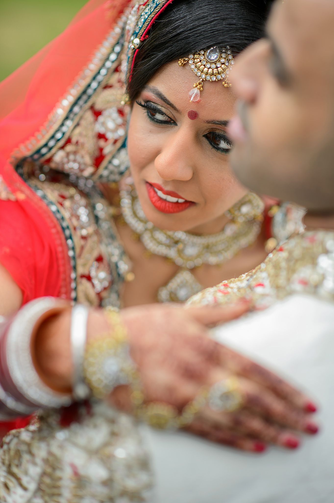 Close up details of ornate bridal jewelry and makeup in red and gold tones.