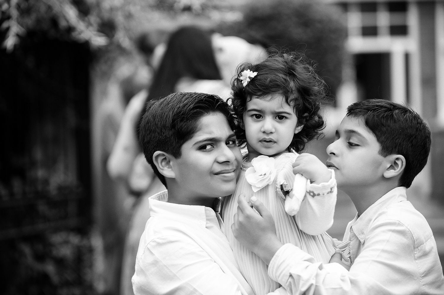Black and white portrait of three young siblings in white shirts.