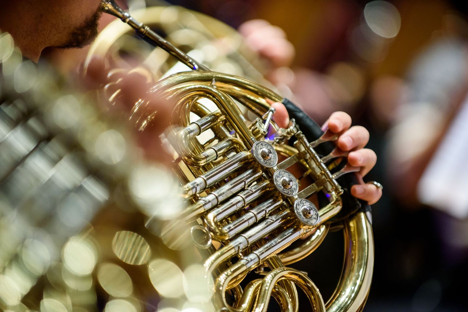 Close-up shot of a brass French horn with beautiful bokeh lighting effects in the background.
