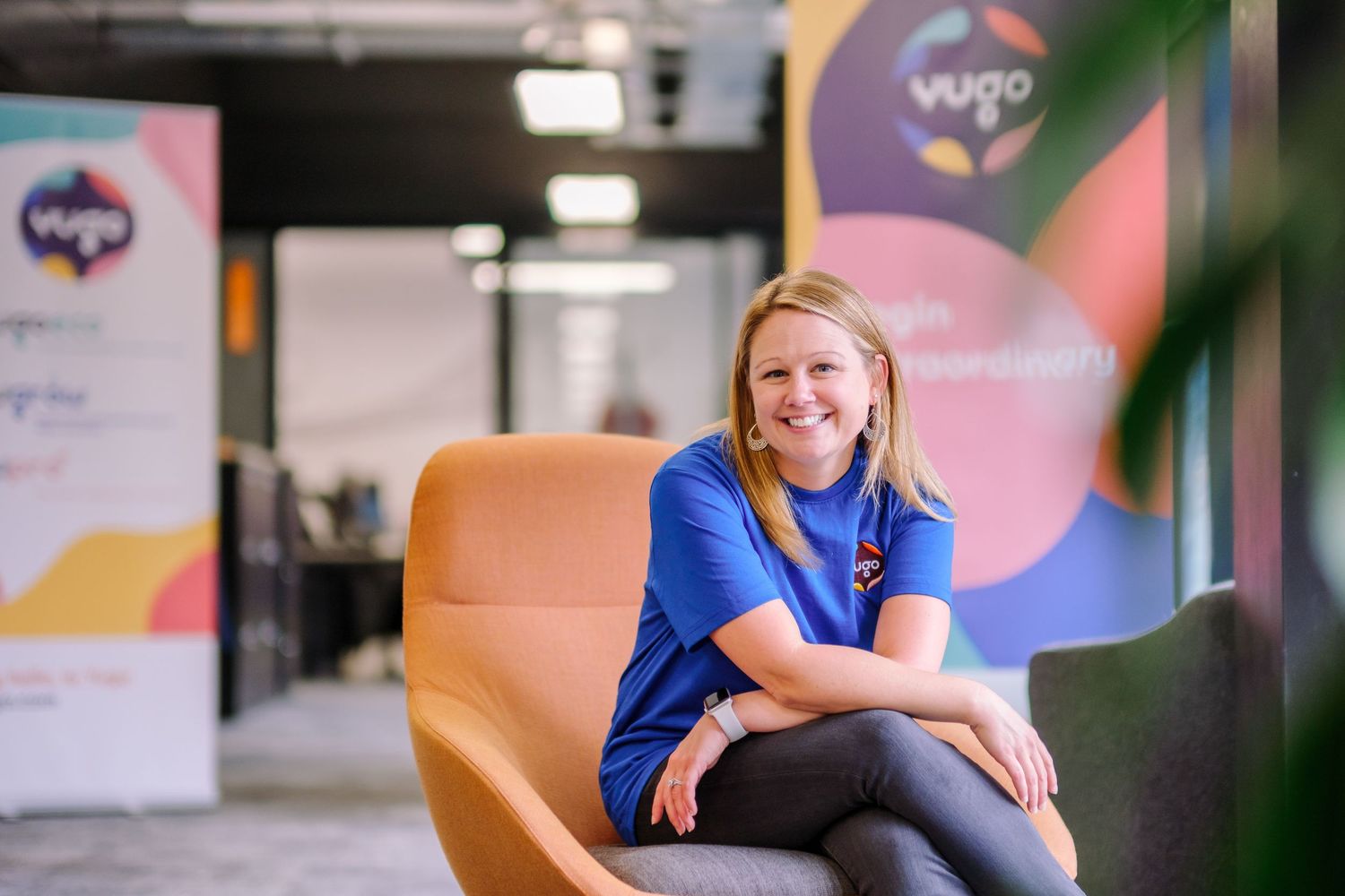 Person in blue shirt sits comfortably on orange chair with colorful office backdrop.