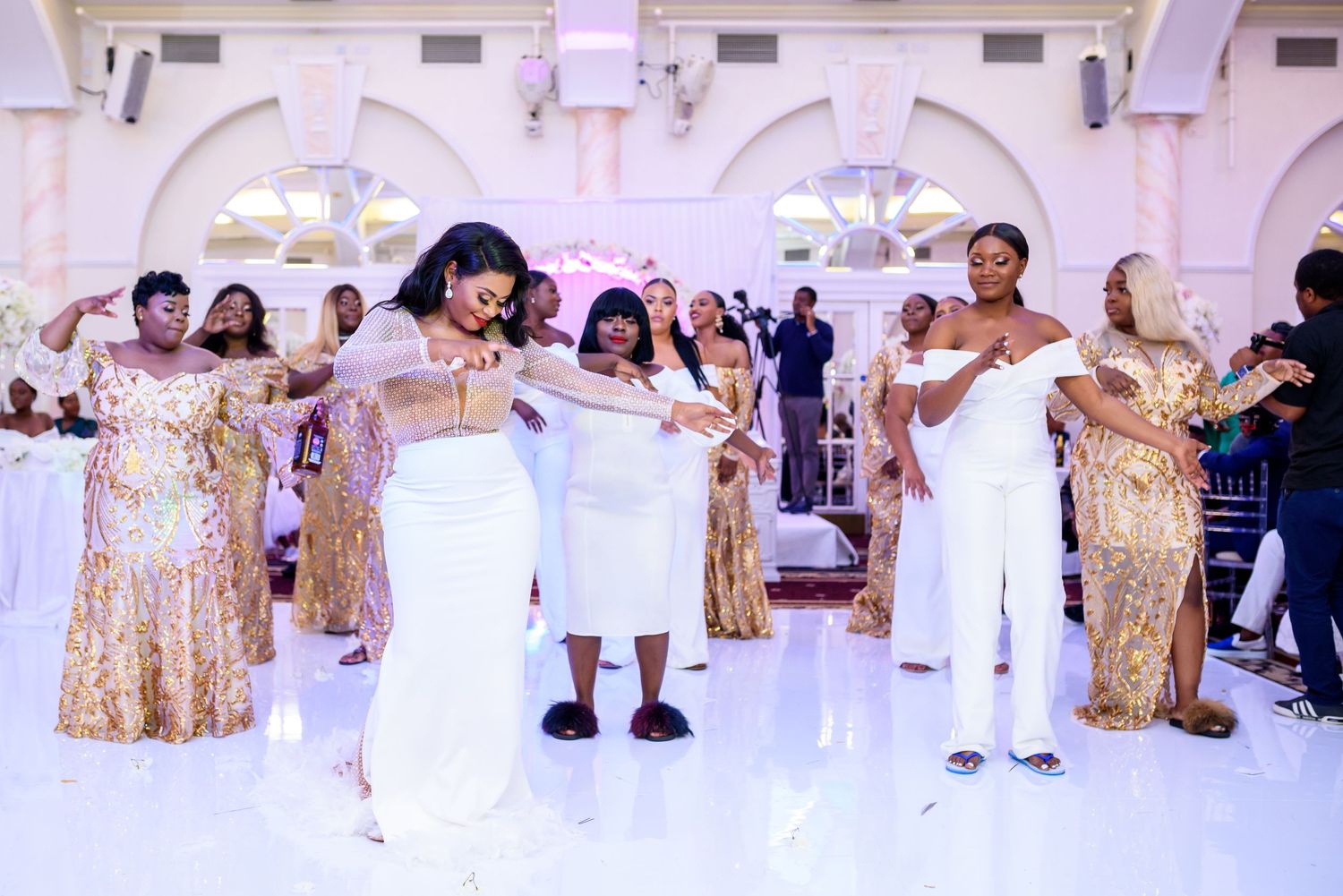 Reception guests in formal attire dancing in an ornate white ballroom with decorative arches.