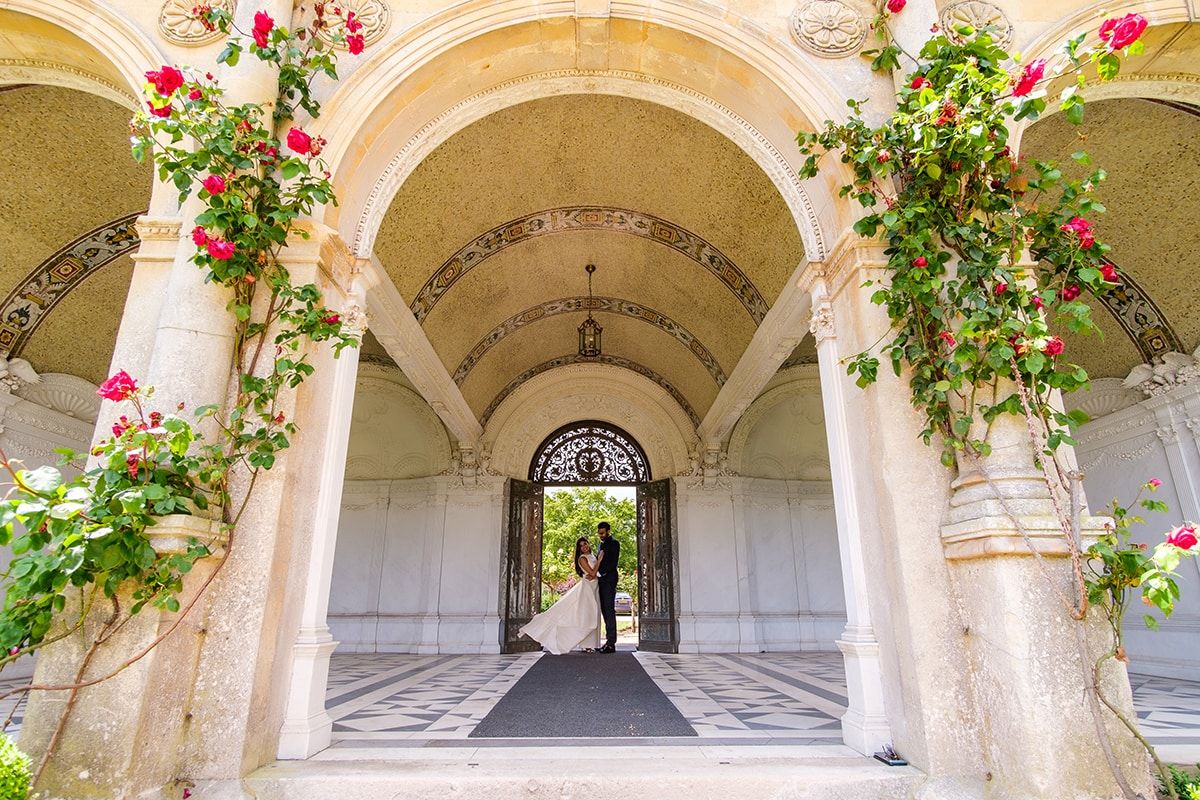 Sunlit stone archways adorned with pink climbing roses and greenery.