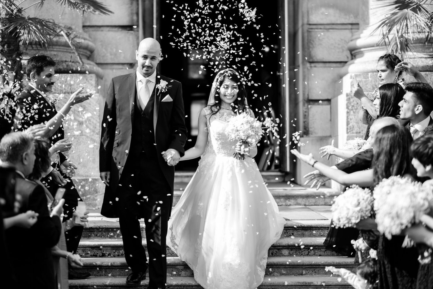 Newlyweds exit their wedding ceremony while guests shower them with confetti.