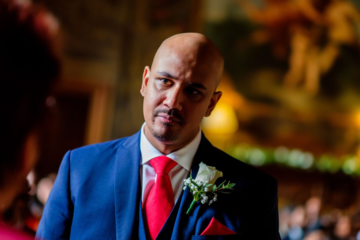 Groom in blue suit and red tie captured in dramatic lighting at wedding reception.