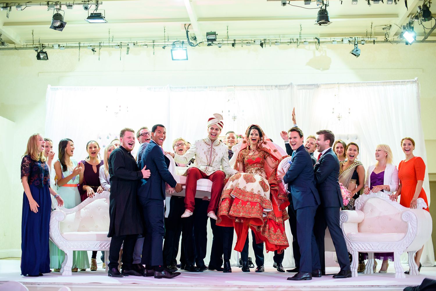 Large group of wedding guests lined up in colorful formal attire at a reception venue.