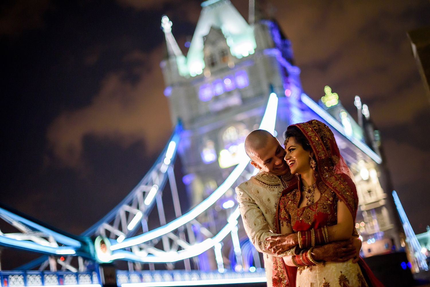London's Tower Bridge illuminated at night with blue lights reflecting on the Thames River.