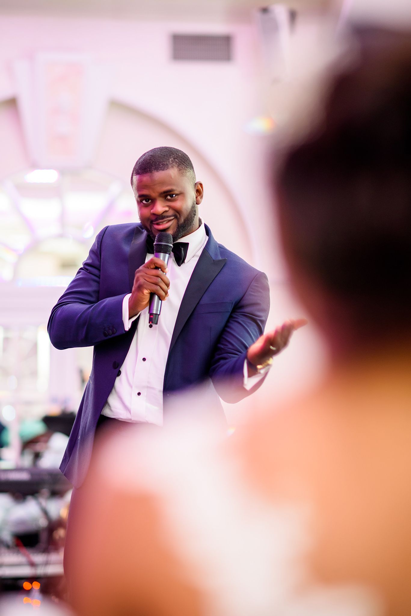 Wedding guest in navy suit delivers a speech with microphone at the reception.