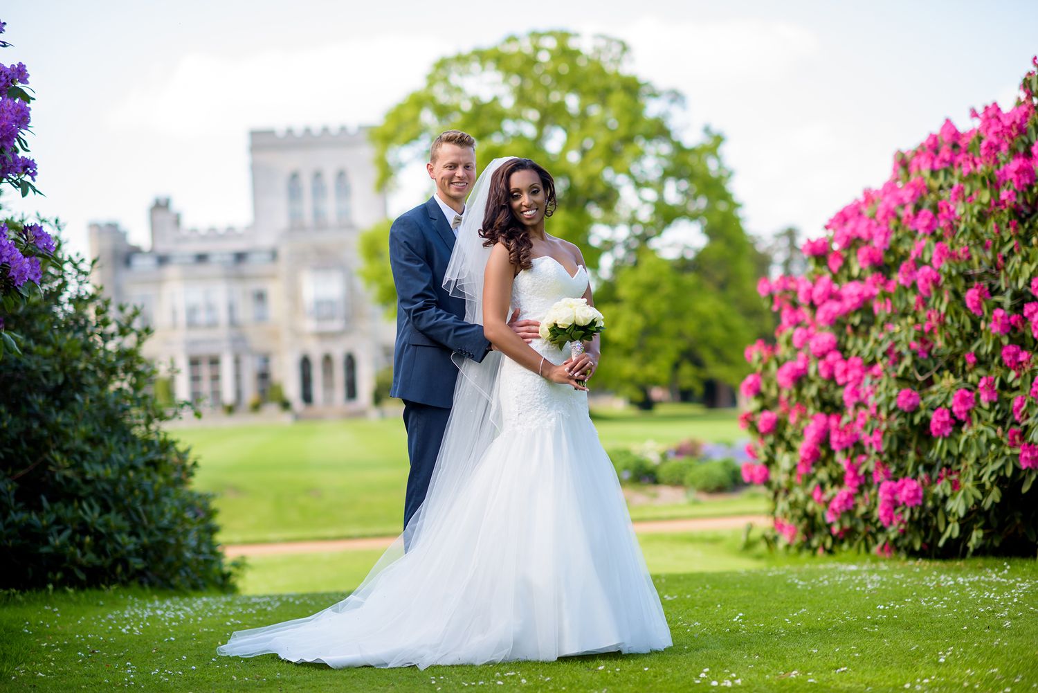 Elegant wedding photography on castle grounds with flowering bushes.