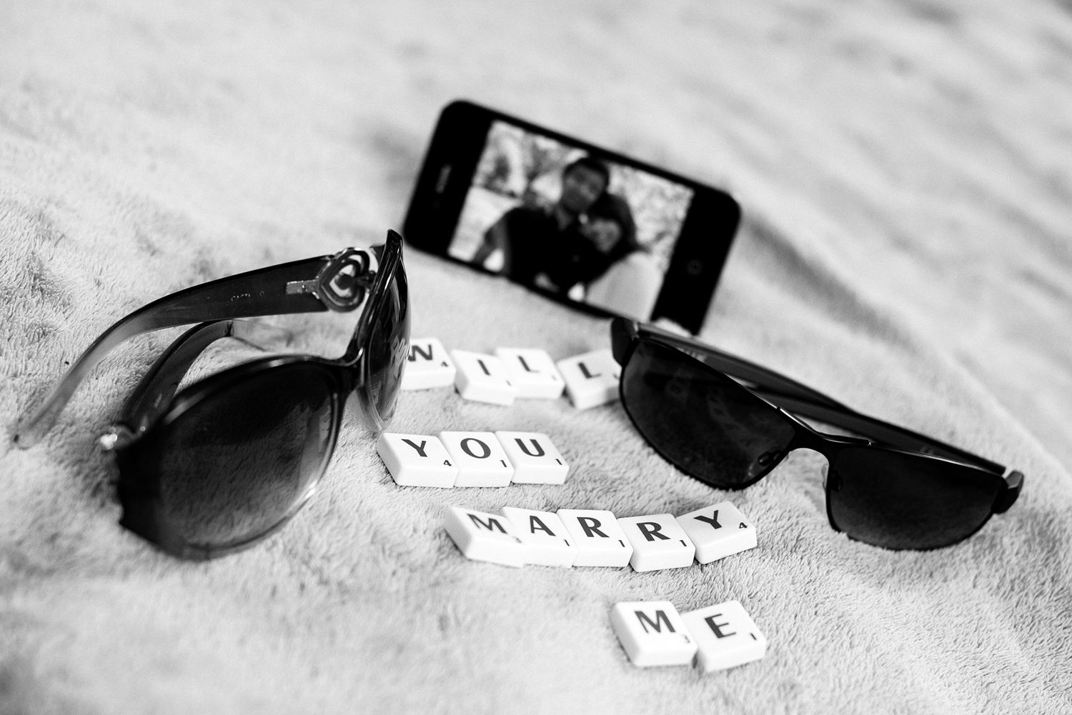 Black sunglasses next to scattered Scrabble letter tiles on a light surface.
