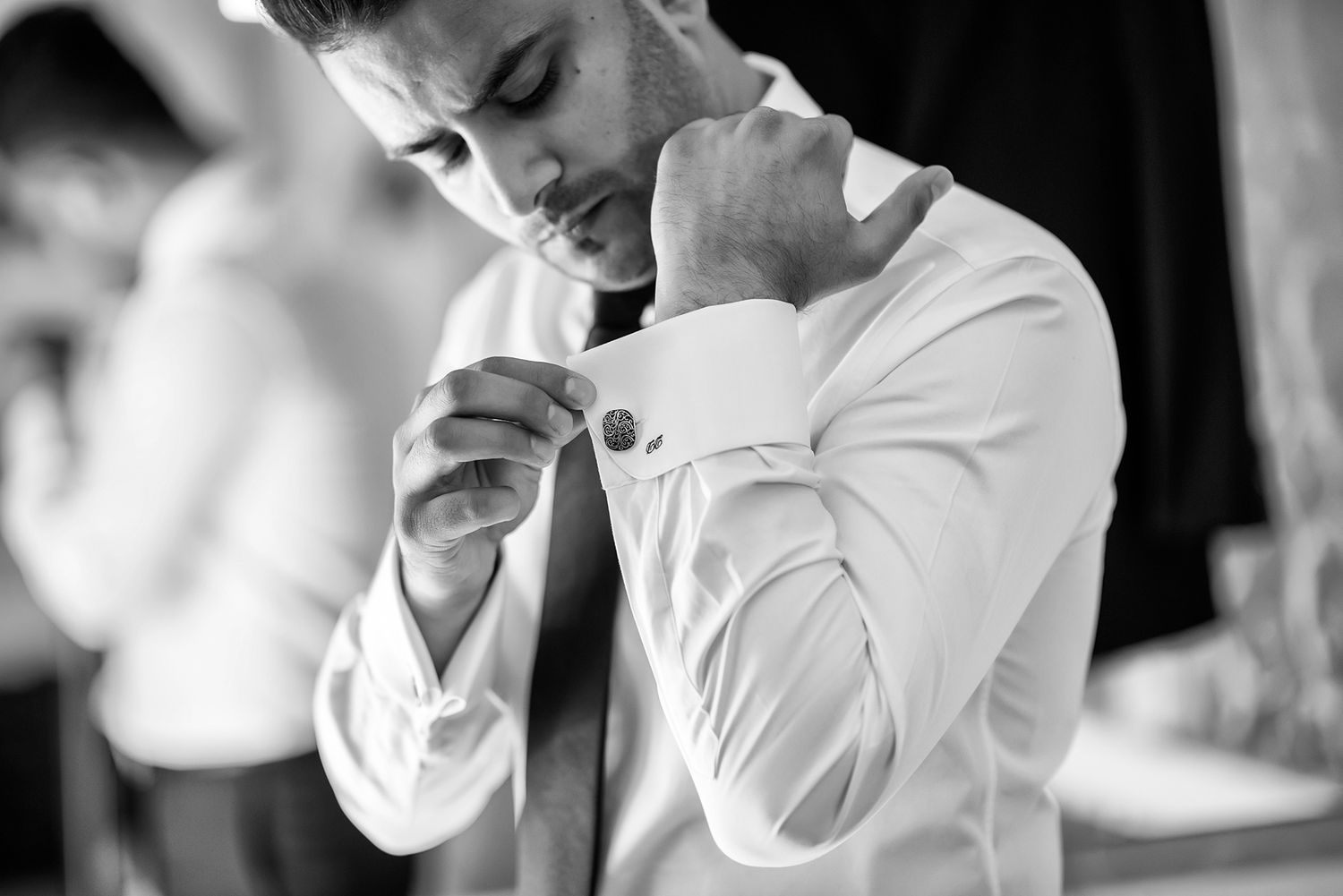 Black and white image of formal preparation showing buttoning of dress shirt.