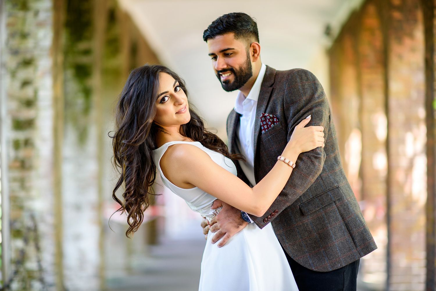 Romantic couple poses in golden sunlight against natural foliage backdrop.