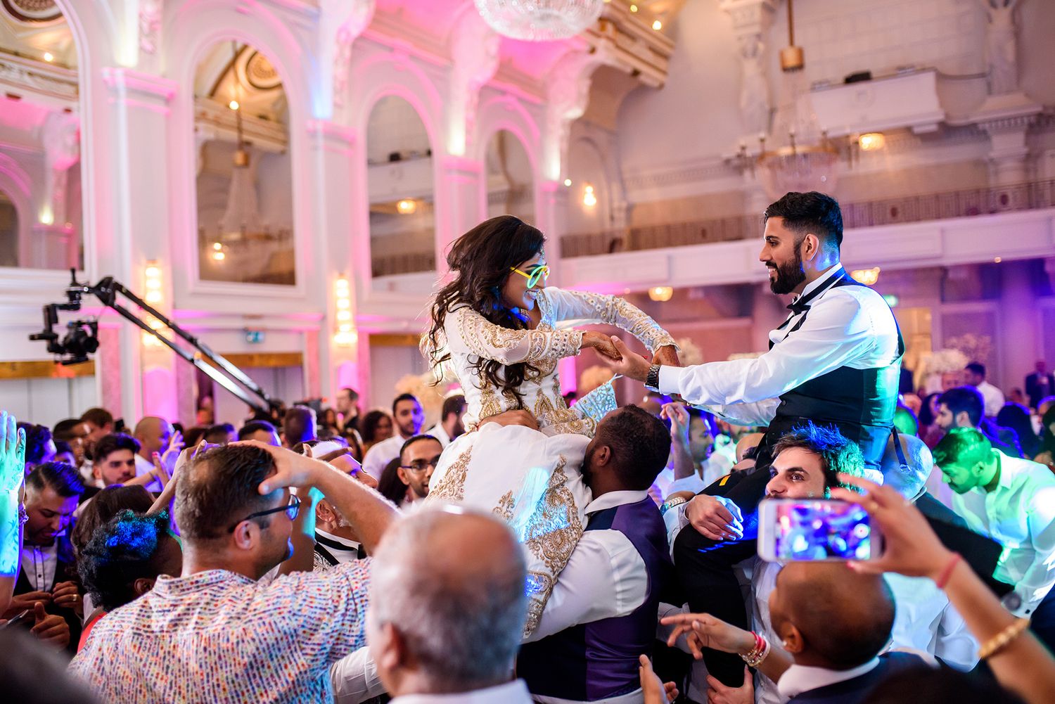 Celebration in a grand ballroom with pink and purple ambient lighting.