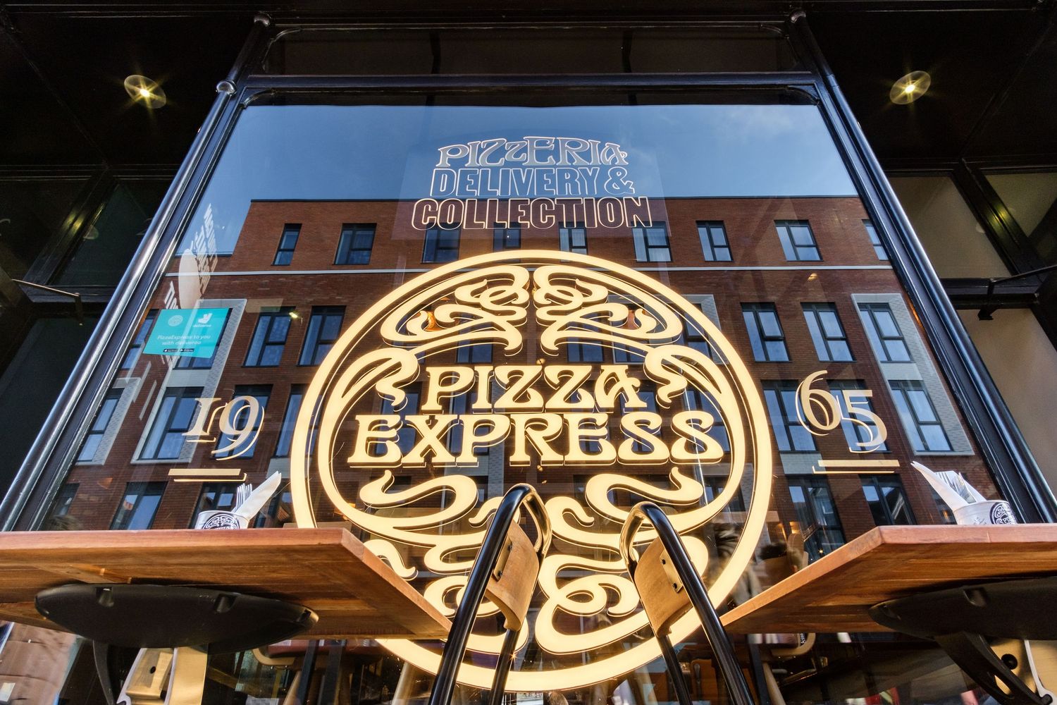 Illuminated Pizza Express logo and signage on dark storefront at night.