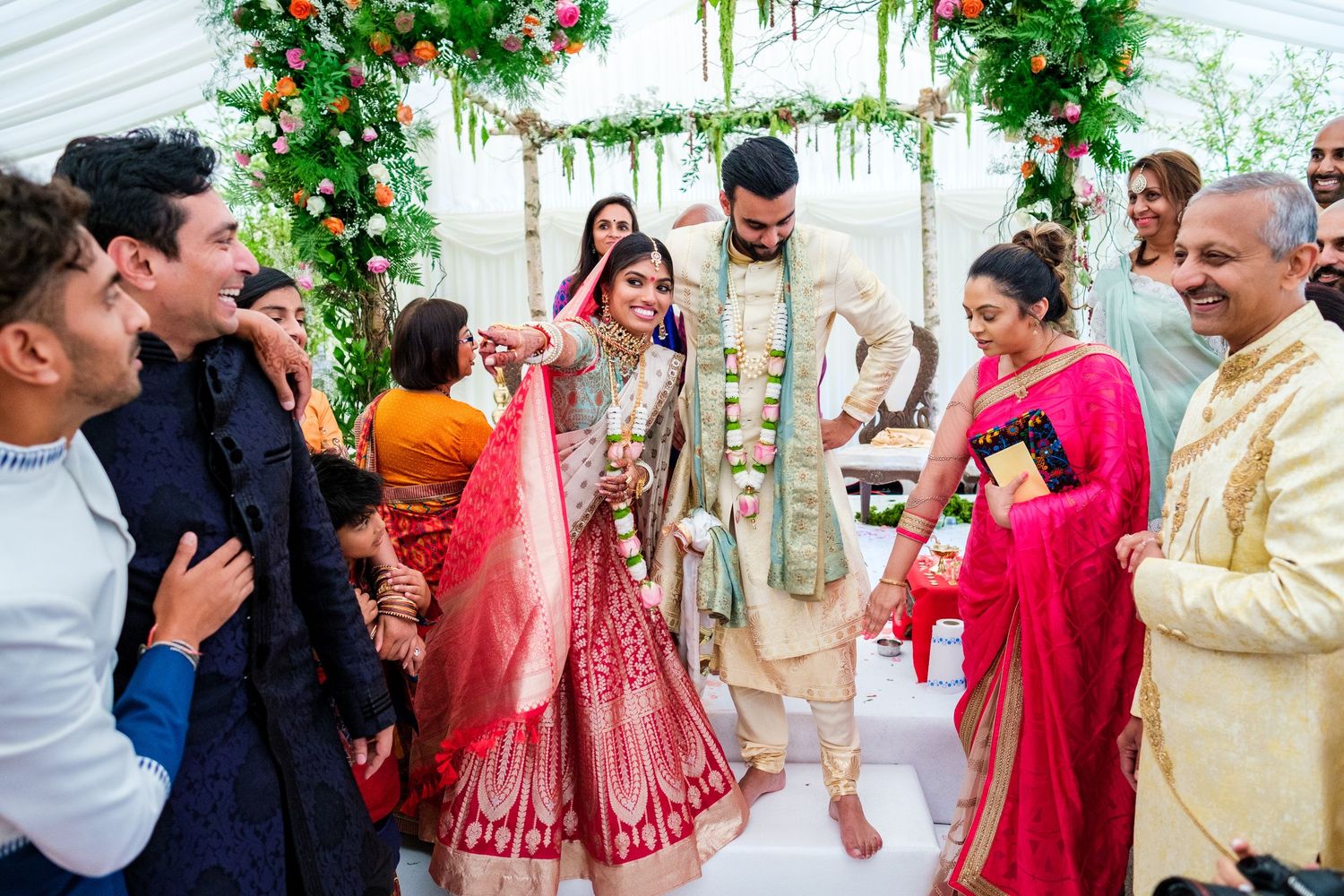 Festive celebration under a decorated tent with red and green floral arrangements during an Indian wedding.