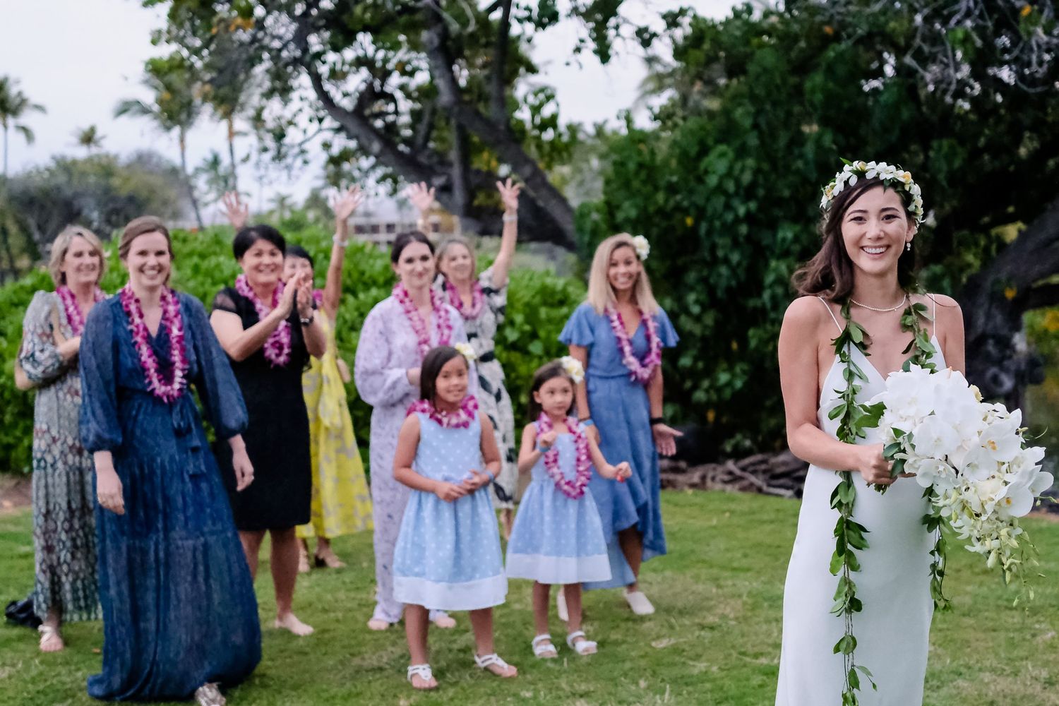 Wedding guests celebrate and dance outdoors at a garden reception party with lush greenery in the background.