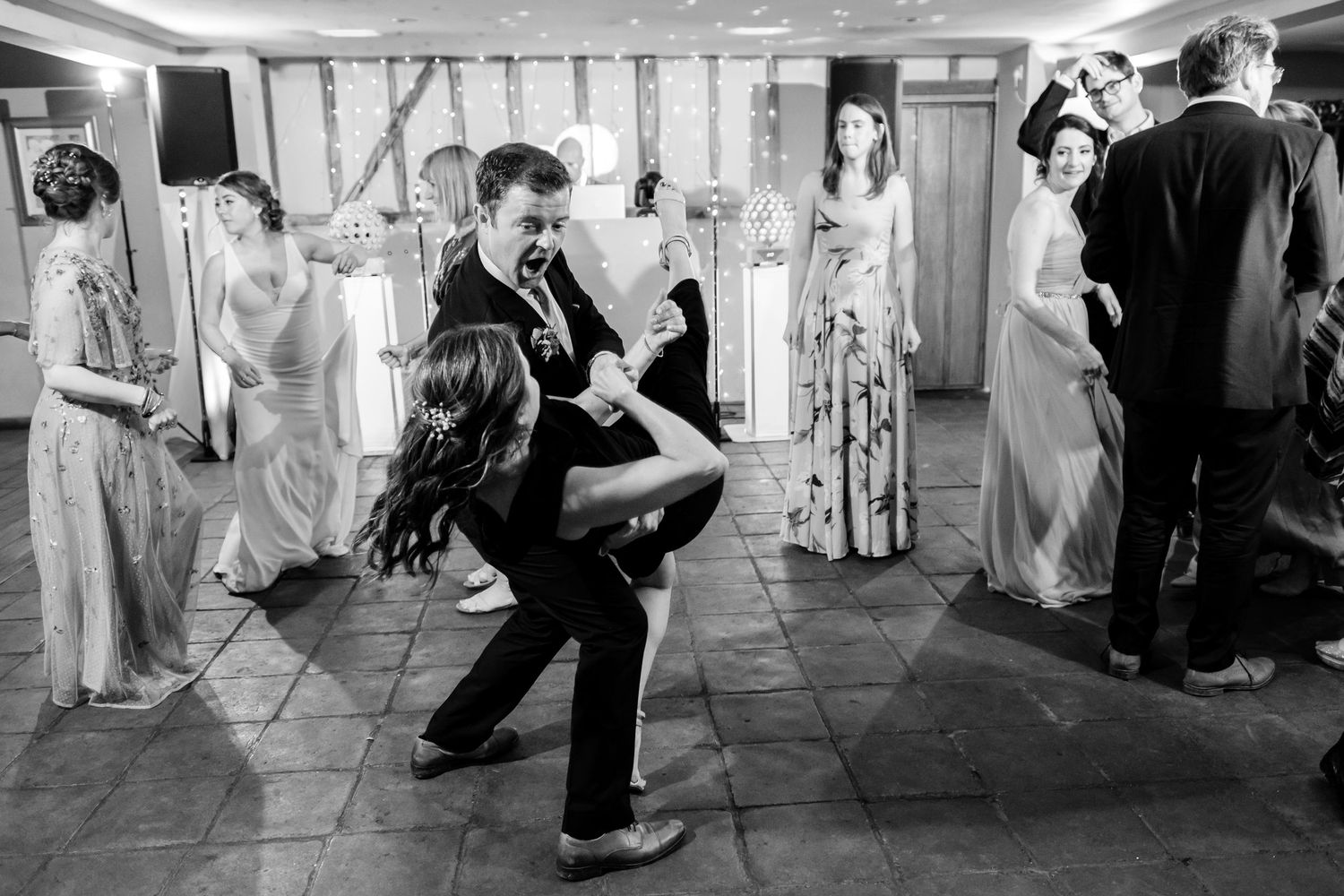 Black and white photo of wedding guests dancing in formation during a reception celebration.