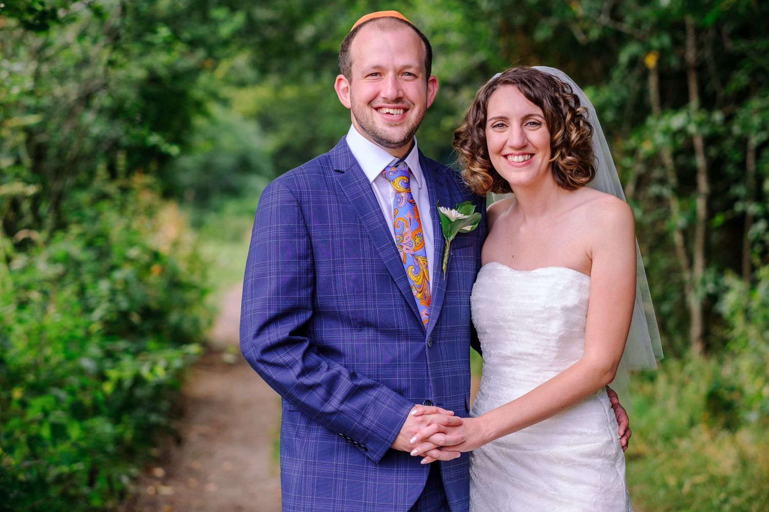 Wedding couple poses together outdoors in a lush green garden setting.