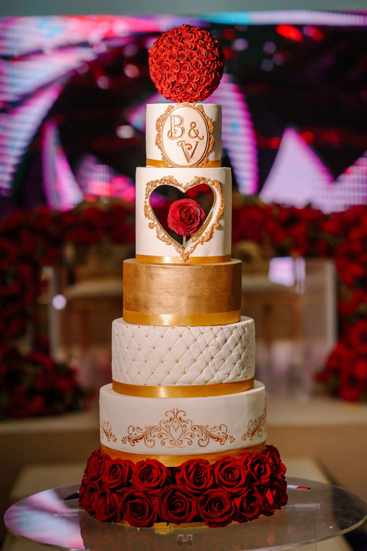 Elegant wedding cake decorated with gold details, red roses and intricate patterns.