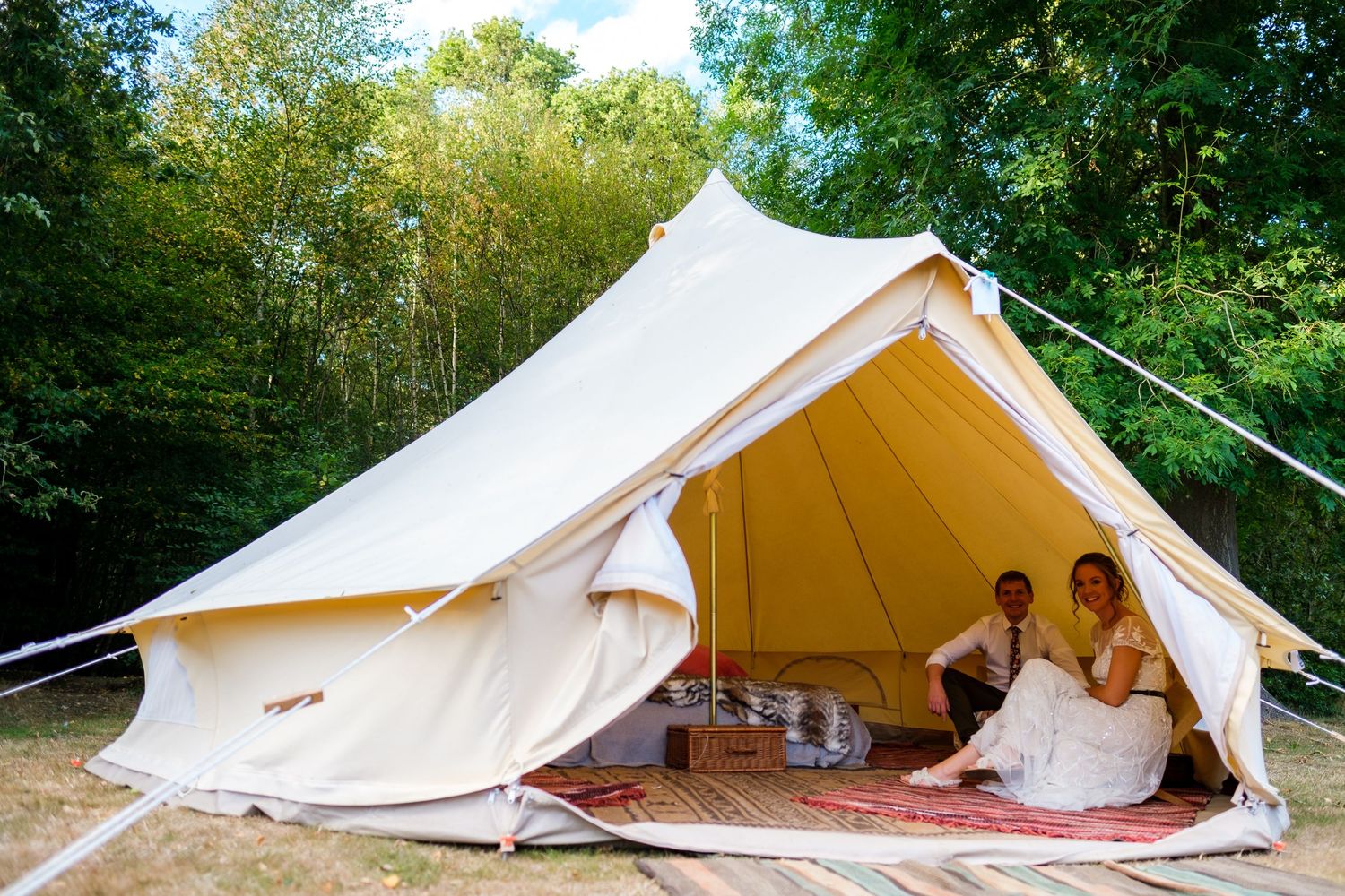 Row of white bell tents set up in a woodland setting for a glamping wedding.