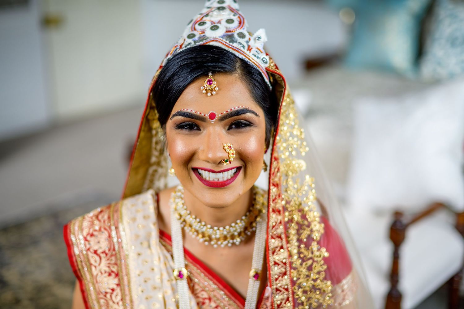 A bride in traditional Indian wedding attire adorned with gold jewelry and embroidered red and gold saree.