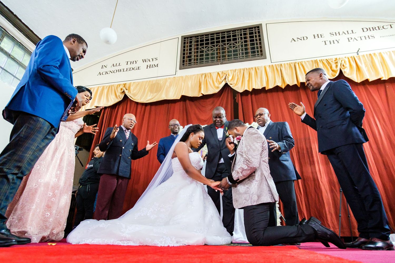 Wedding ceremony taking place on a red carpet with decorative curtains in the background.