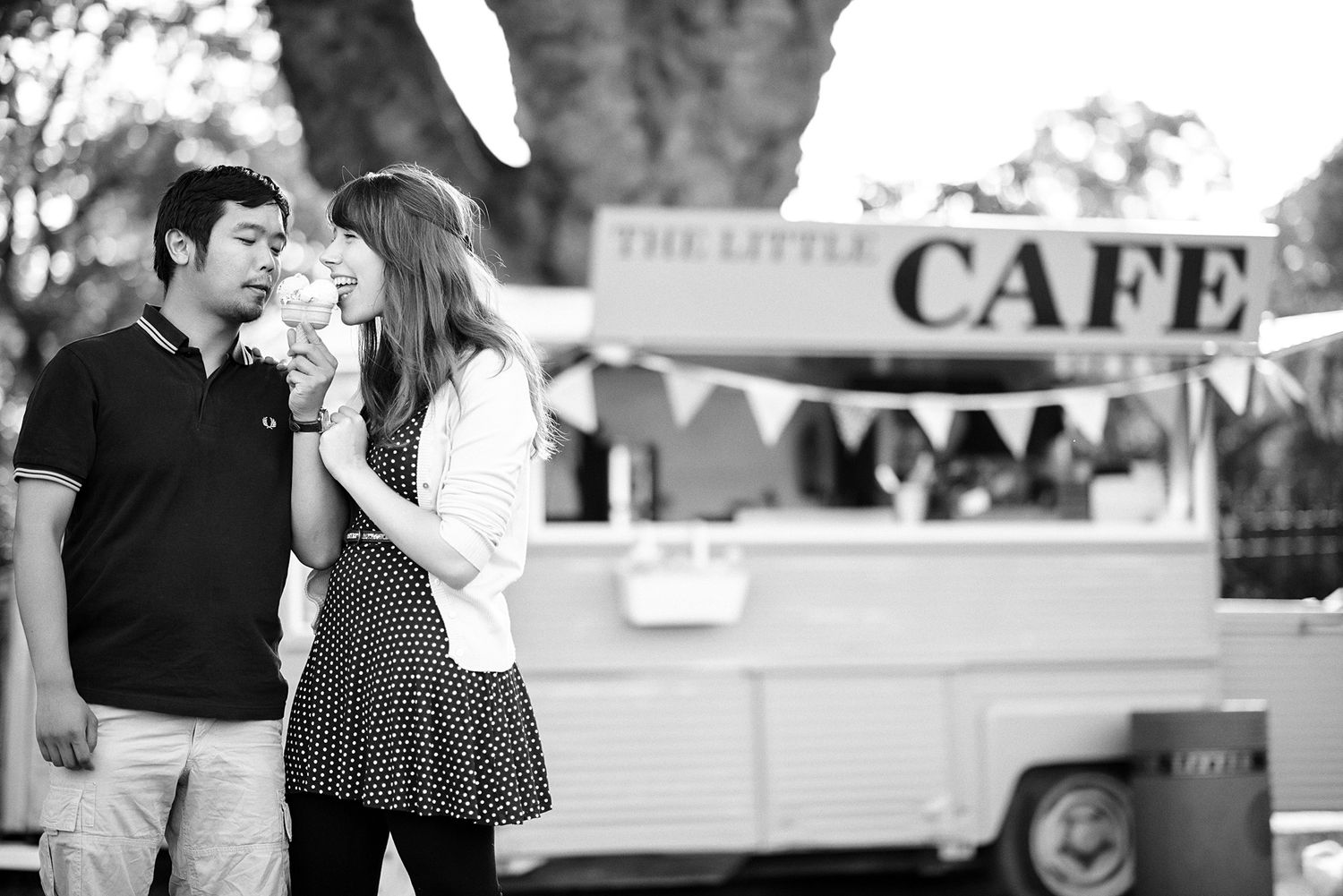 A black and white photo of a couple standing near a cafe food truck sharing a romantic moment.