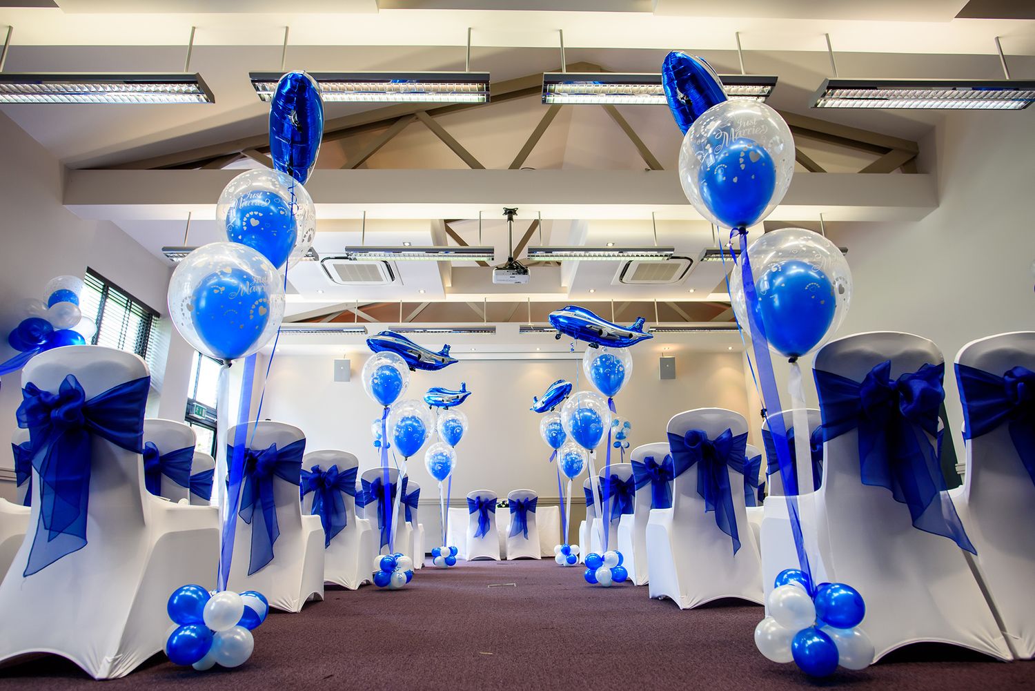 Indoor event space decorated with blue and white balloons for a celebration.