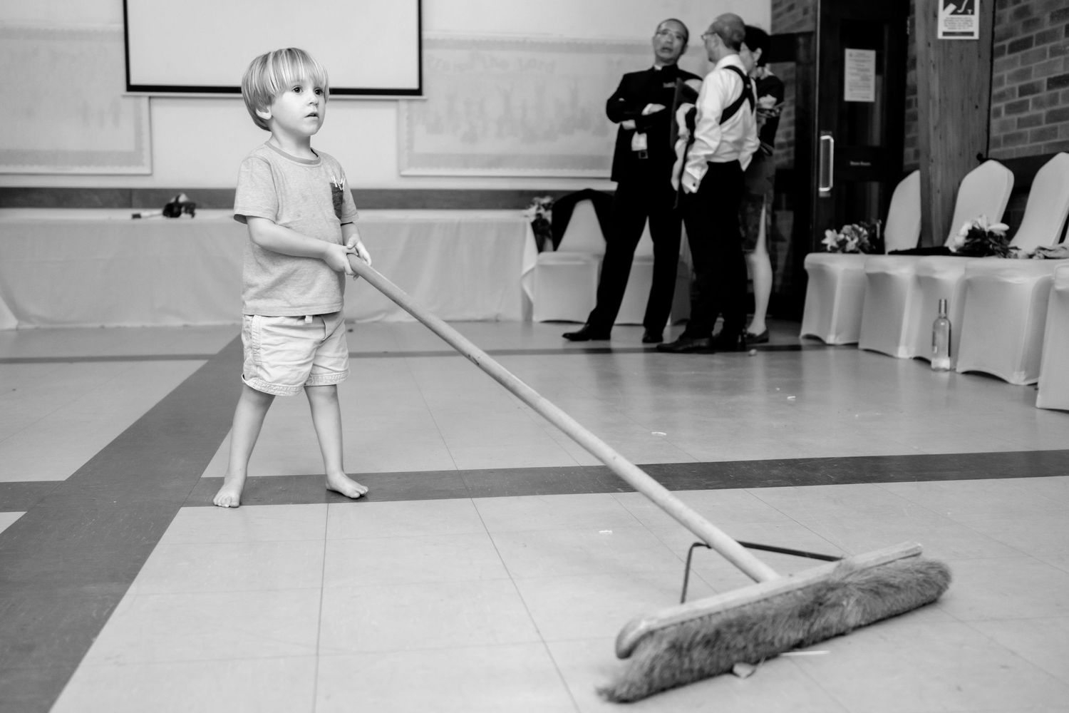 Person cleaning a hardwood floor with a large industrial mop in a commercial space.