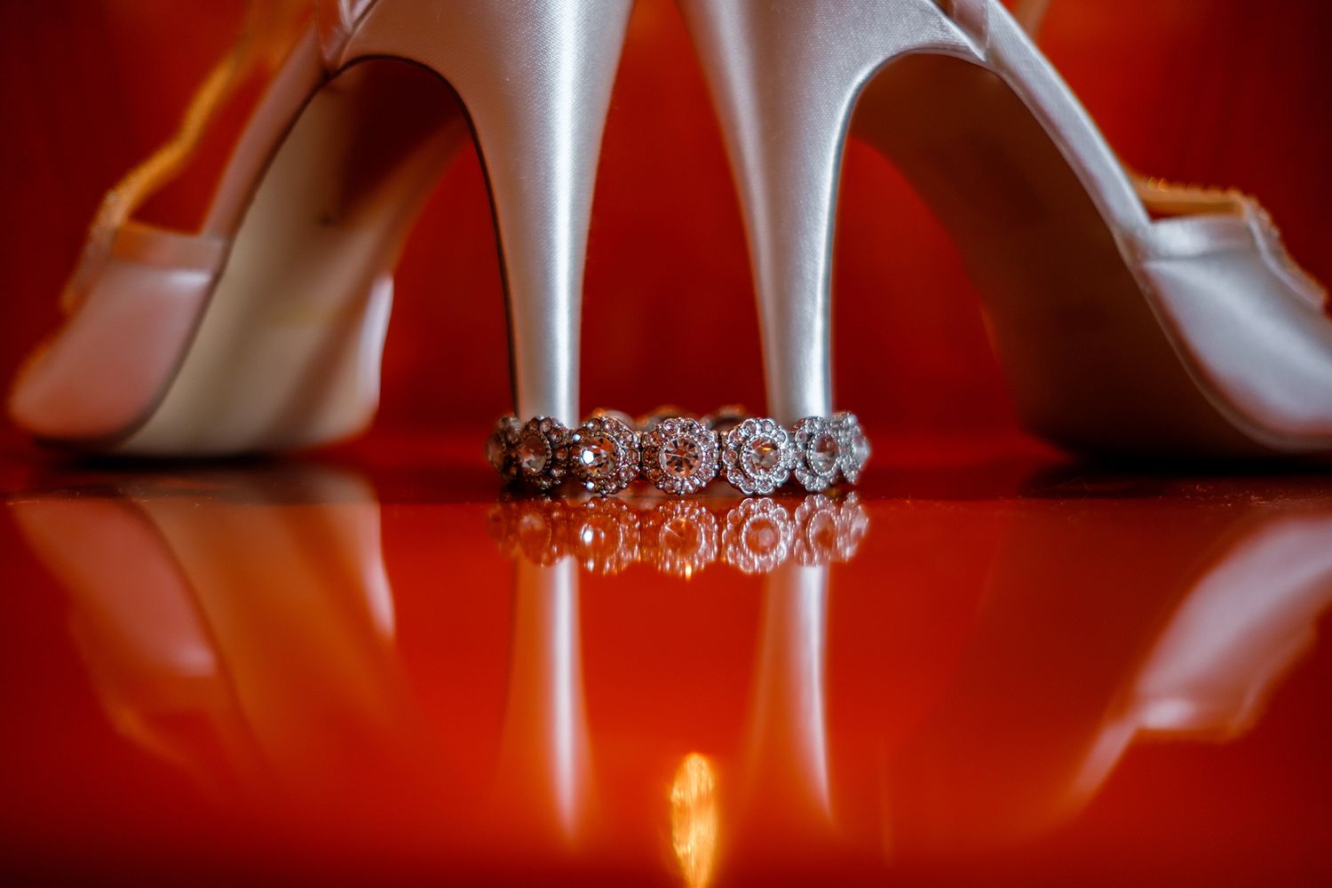 Close-up shot of elegant white high heels with crystal details on reflective red surface.