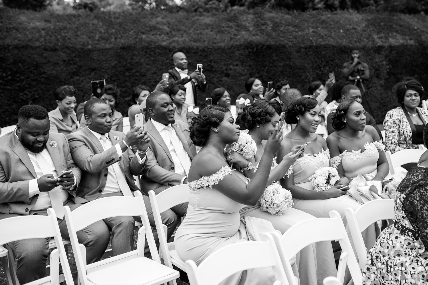 Wedding guests seated in rows of white chairs during an outdoor garden ceremony.