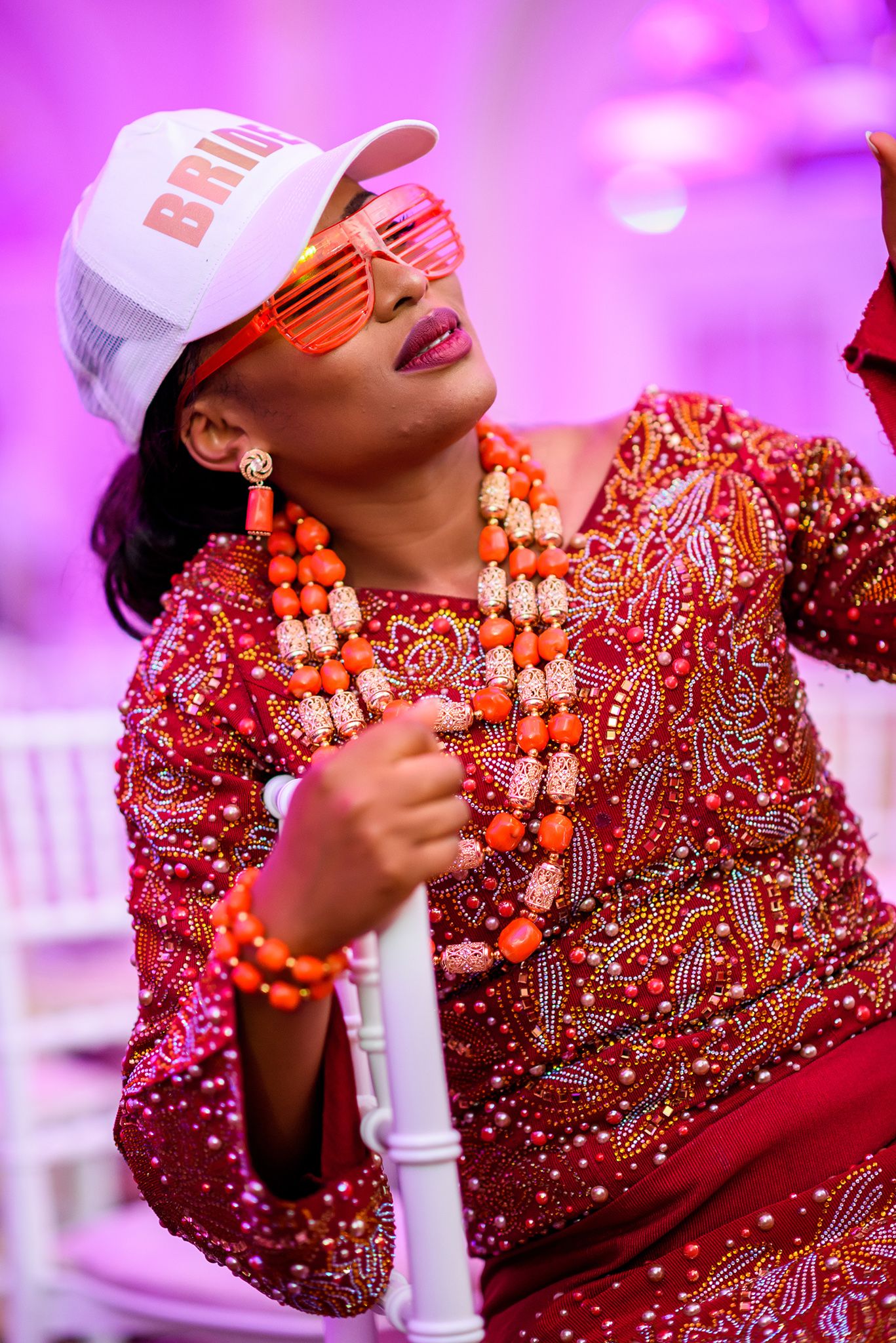 Close-up details of ornate red and gold beaded traditional wedding attire under purple lighting.